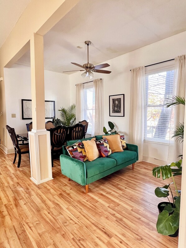 A spacious living room with a green sofa, wooden flooring, and a ceiling fan. - Big Groups Central Memphis stay-5BR/4BA w/Parking - Walk to FedEx Forum&Beale St (Memphis)