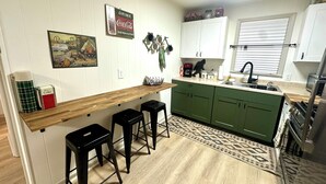 Une cuisine avec un comptoir-bar en bois, des armoires vertes, une machine à café et un évier.