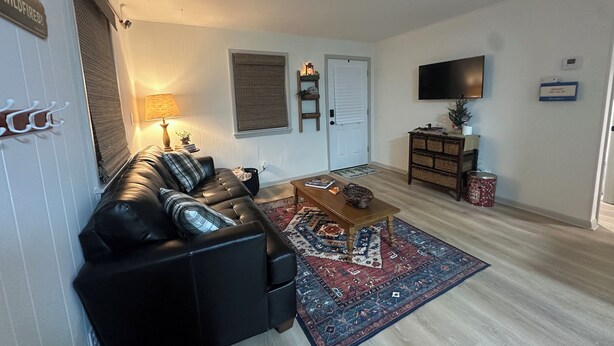 Un salon avec un canapé en cuir noir, une table basse en bois, un tapis à motifs, un téléviseur et un petit meuble.