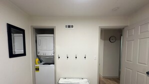 Une petite pièce comprenant un lit, une petite table, un lave-linge et une horloge murale.