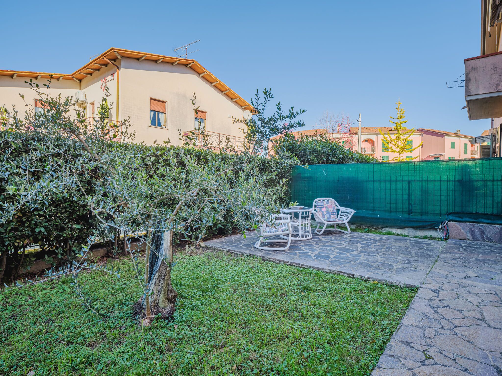 A courtyard with a stone patio, outdoor furniture, and a green fence.