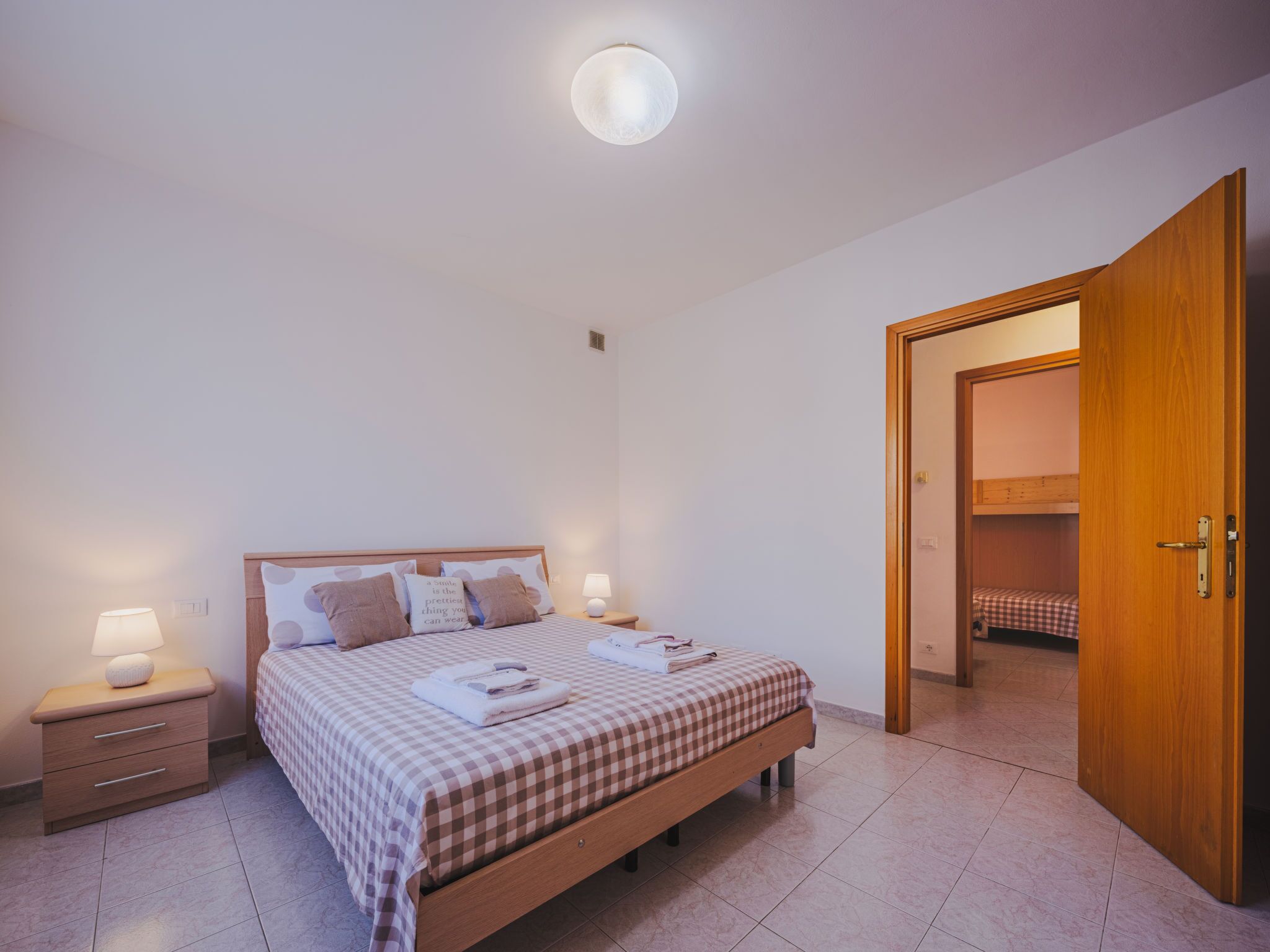 A bedroom with a bed, bedside tables, a nightstand, a wooden door, and a view into another room.