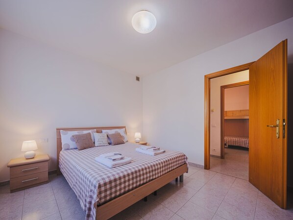 A bedroom with a bed, bedside tables, a nightstand, a wooden door, and a view into another room.