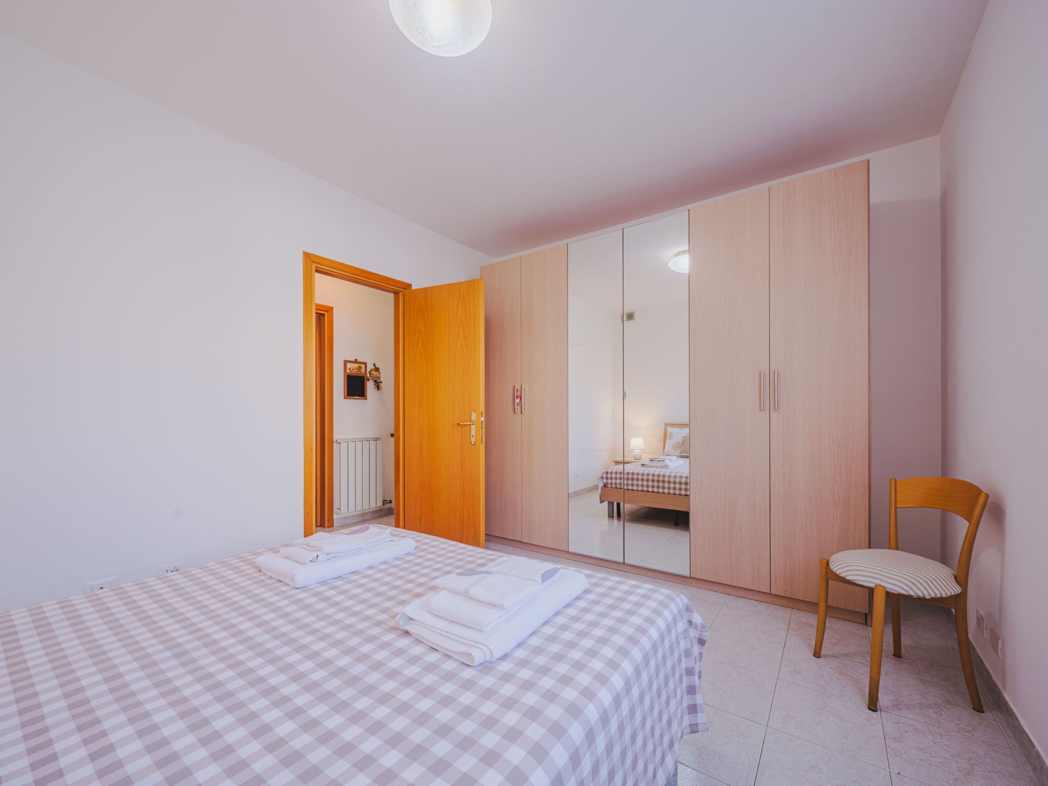 A bedroom with a bed, a chair, a wardrobe, and a mirror.