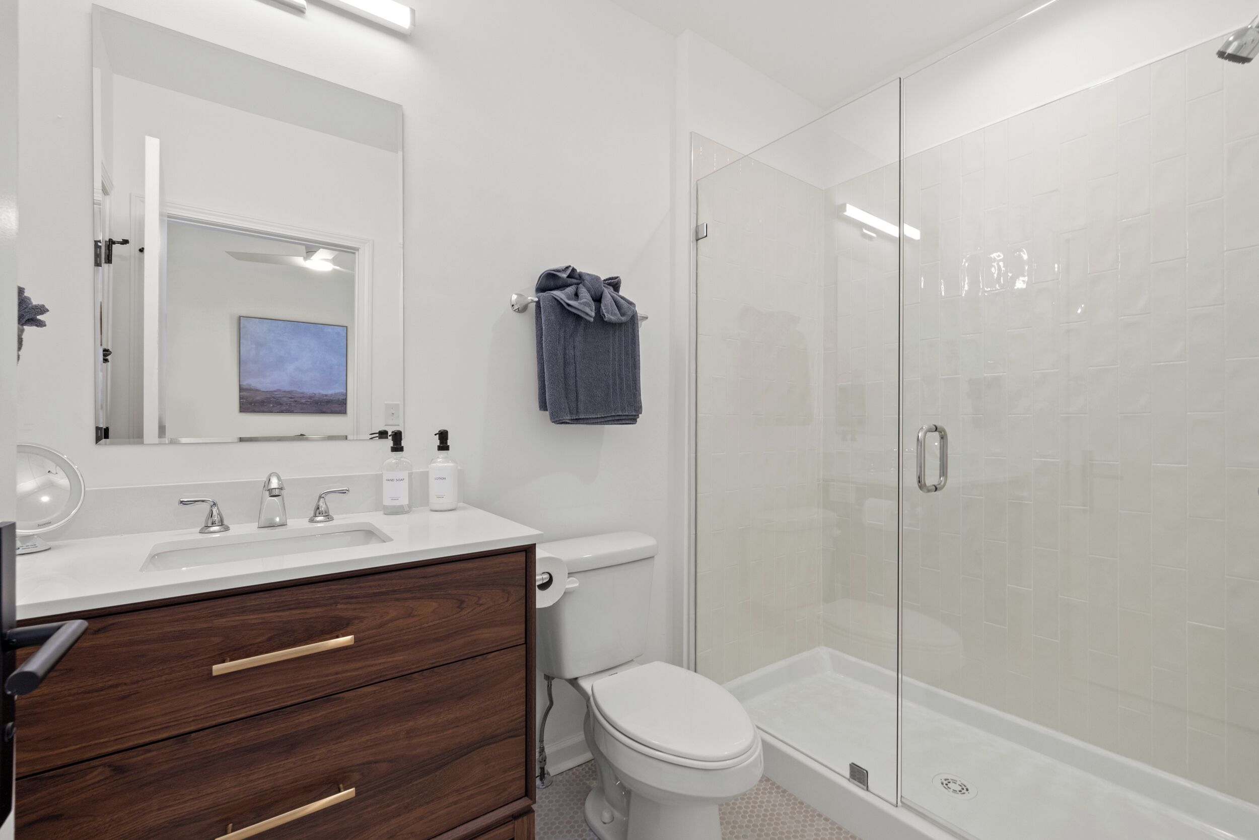 A modern bathroom with a white sink, wooden vanity, a toilet, and a glass-enclosed shower.