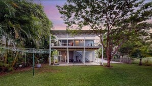 A modern two-story house with a flat roof, surrounded by a well-maintained lawn and trees. - Charming Queenslander in Beachmere: WiFi, A/C, Netflix, Kayo, Sleeps up to 10. (Beachmere)