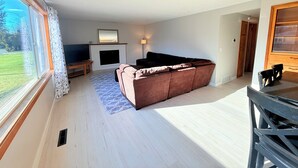 Ein Wohnzimmer mit einer Couch, einem Kamin, einem Fernseher und einem Fenster mit Vorhängen.