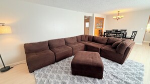 Ein modernes Wohnzimmer mit einem Ecksofa, einem passenden Hocker und einem gemusterten Teppich.