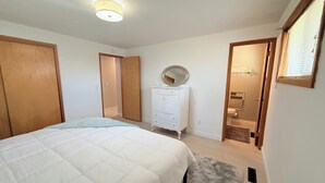 Ein Schlafzimmer mit Bett, Kommode, Spiegel und einem durchgegangenen Tür angedeuteten Badezimmer.