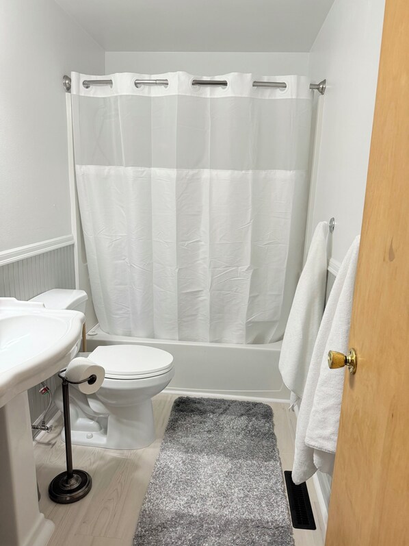A bathroom with a toilet, sink, shower curtain, and a towel hanging on the door.