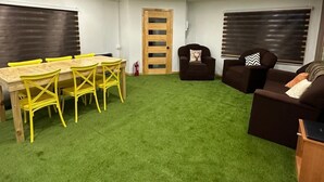 Una habitación con alfombra verde, una mesa de madera con sillas amarillas, un sofá marrón y una puerta de madera.