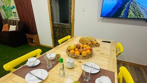 Un comedor con una mesa de madera dispuesta para cuatro, sillas amarillas y un televisor en la pared mostrando una vista panorámica.