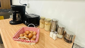 Una encimera de cocina con cafetera, tostadora y una cesta de huevos. Hay frascos de cereales y recipientes de sal.