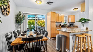 A modern kitchen with wooden cabinets, a granite countertop, and a dining area with a wooden table and black chairs.