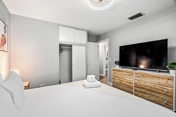 Un dormitorio moderno con una cama grande, televisor, cómoda de madera y vestidor.