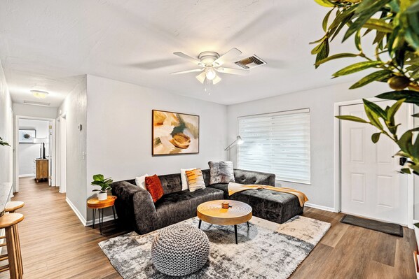 A modern living room with a dark leather sofa, a round wooden coffee table, and a ceiling fan.