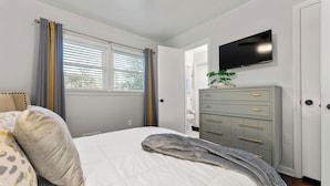 Ein Schlafzimmer mit einem Bett, einem Schminktisch, einem Fernseher und einem Fenster mit Vorhängen.