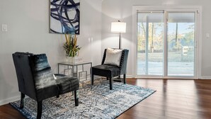 Ein modernes Wohnzimmer mit zwei schwarzen Ledersesseln, einem gemusterten Teppich, einer Stehlampe und einem großen abstrakten Gemälde an der Wand.