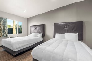 A hotel room with two beds, a large window with curtains, and a view of the outdoors. - Suburban Studios Ridgecrest near China Lake Naval Station (Ridgecrest)