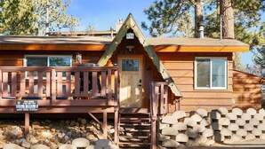 Une cabane avec une terrasse en bois, une cheminée et une boîte aux lettres.