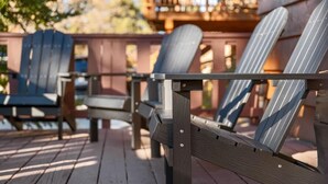 Une terrasse en bois, dotée de chaises Adirondack et d’une rambarde en métal.