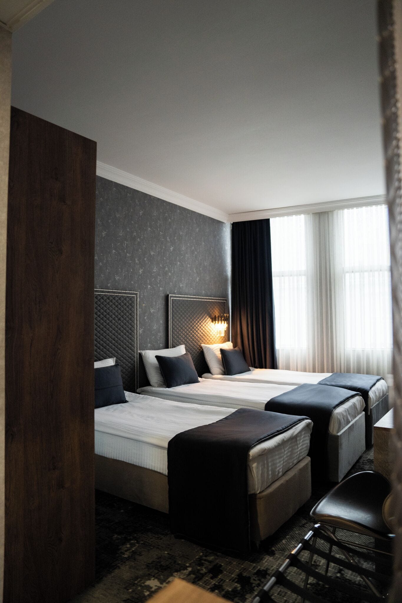 Une chambre d’hôtel avec deux lits, une grande colonne en bois, un mur à motifs et une fenêtre avec des rideaux.