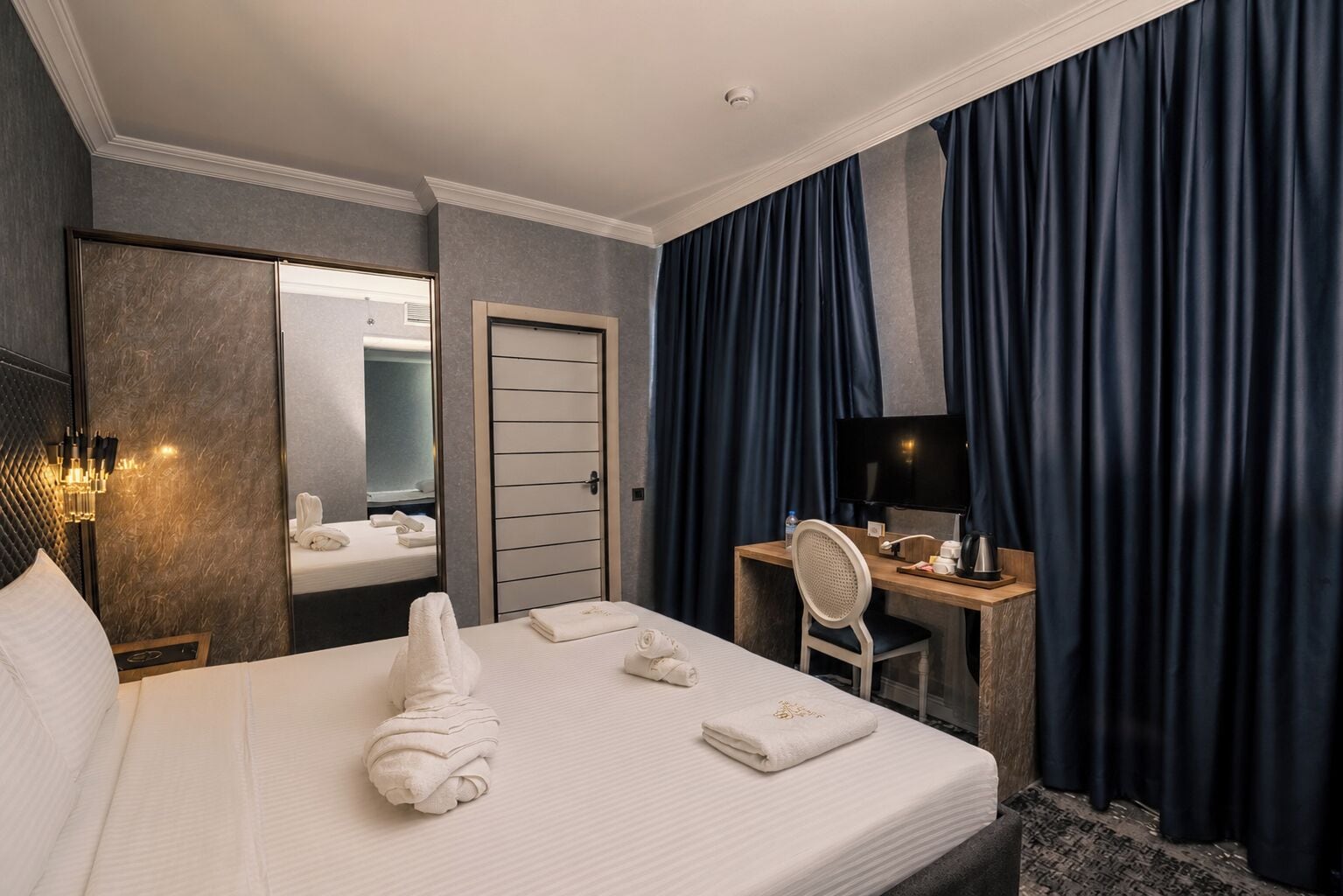 A hotel room with a bed, a desk with a chair, a television, and a mirror.