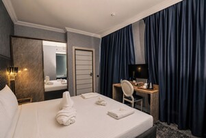 A hotel room with a bed, a desk with a chair, a television, and a mirror.