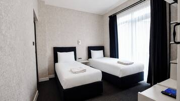 Een hotelkamer met twee bedden, een bureau met een computer en een raam met gordijnen.