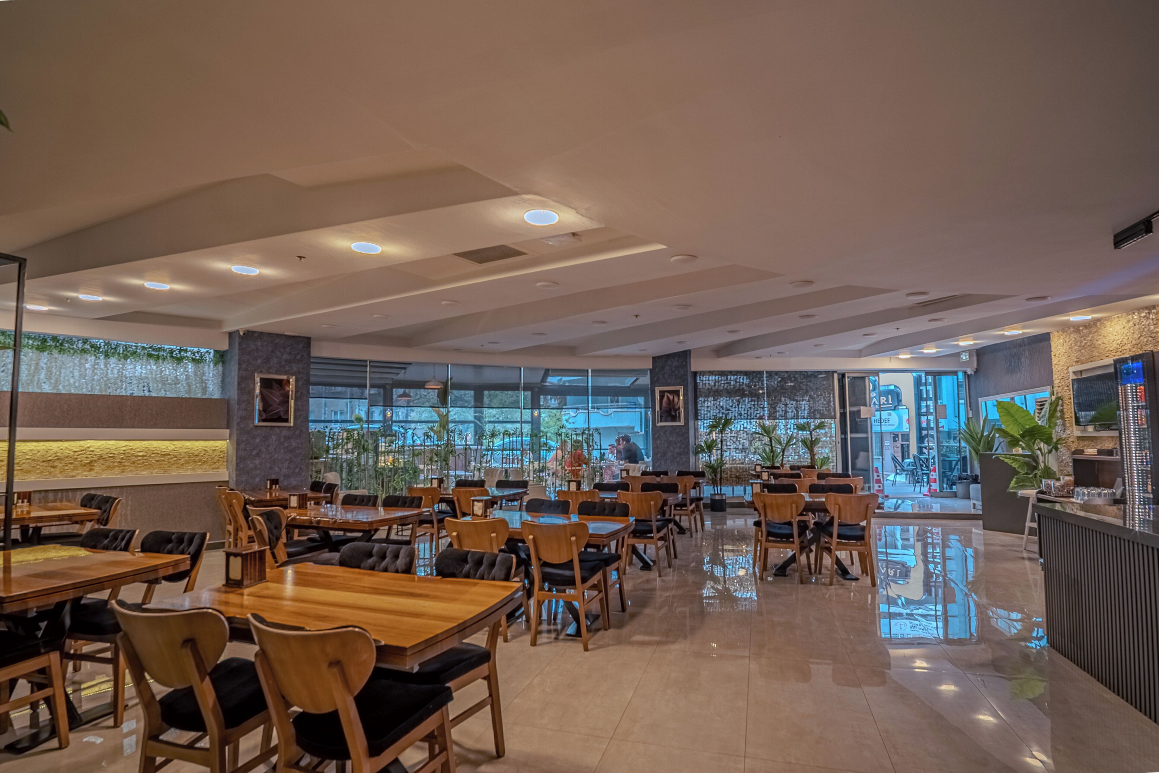 Un interior de restaurante moderno con mesas y sillas de madera, ventanas amplias y una zona de bar central.
