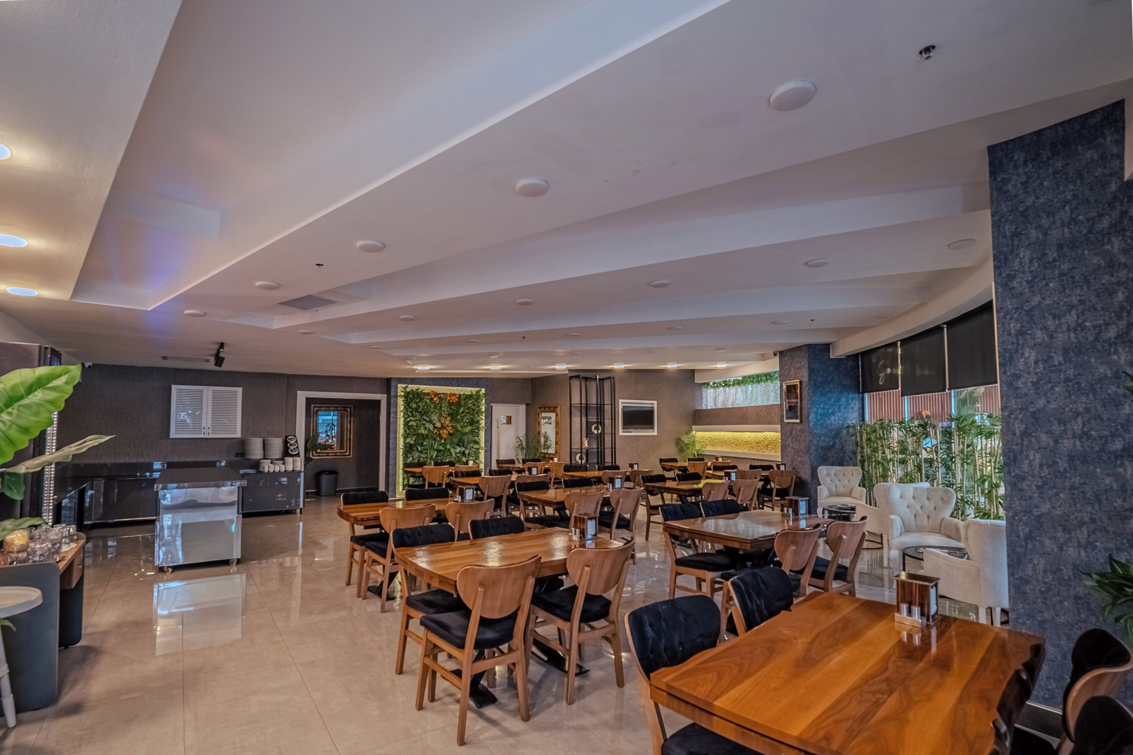 Un comedor moderno con mesas y sillas de madera, una zona de cocina y un espacio de estar con vistas al exterior.