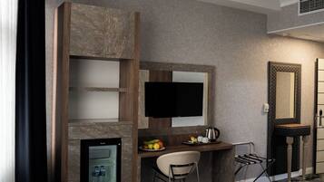 Habitación de hotel con una cama, un escritorio con silla, televisor, espejo y una pequeña área de kitchenette.