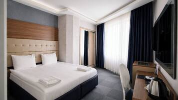 A hotel room with a large bed, a desk with a chair, a television, and a window with curtains.