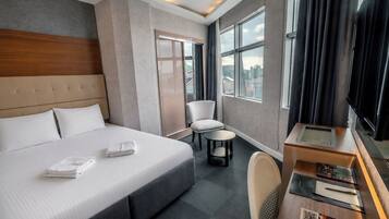 Une chambre d’hôtel avec un grand lit, un bureau équipé d’un ordinateur, une chaise et une vue sur la ville grâce à de grandes fenêtres.