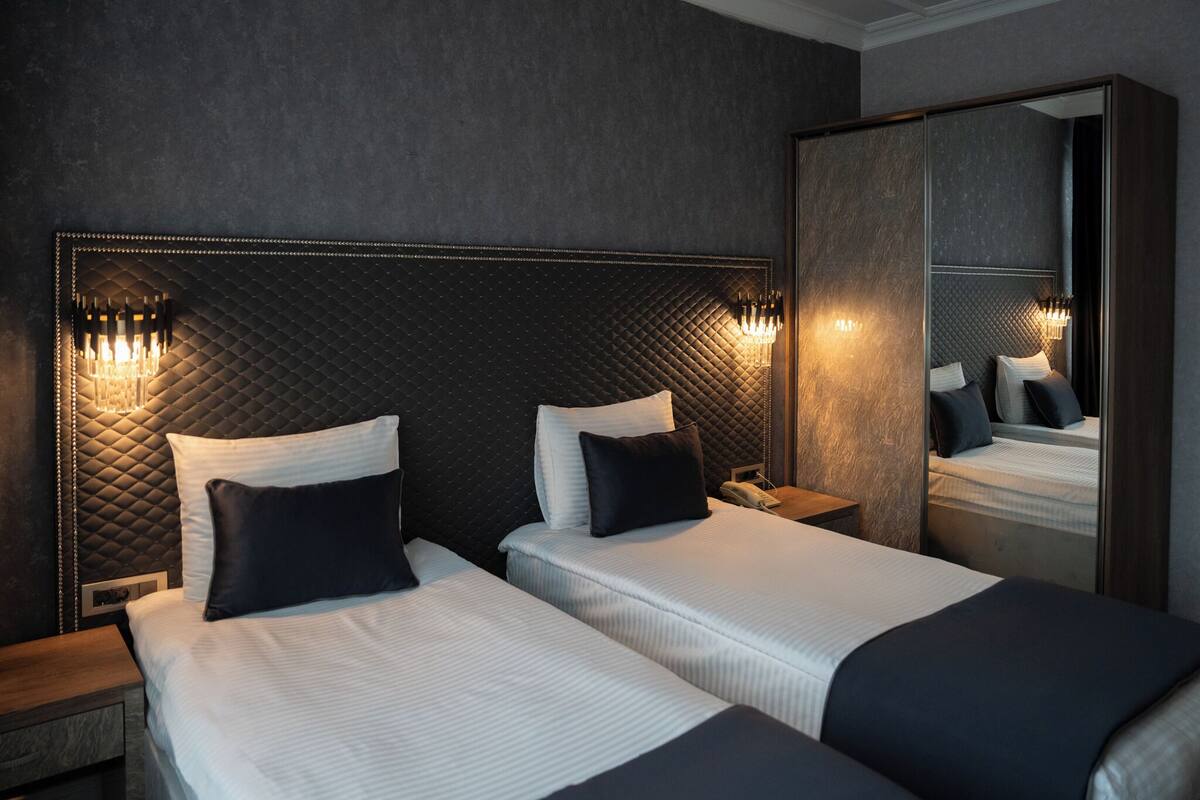 A hotel room with two beds, a large mirror, and wall-mounted sconces.