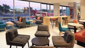 A modern indoor seating area with sofas and chairs, a bar, and large windows offering a view of the street. - avid hotel Guadalajara Aeropuerto Norte by IHG (Tlaquepaque)