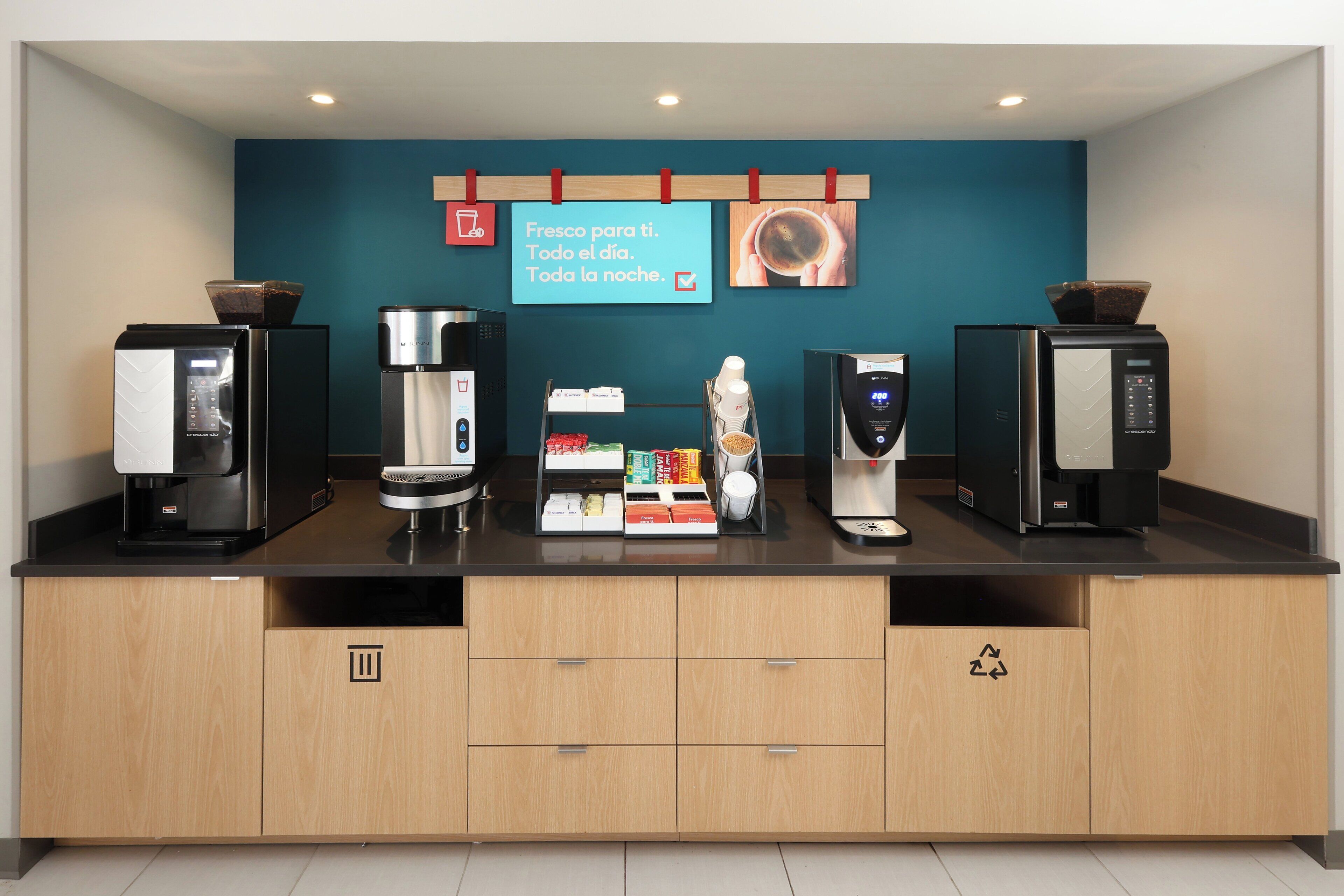 A coffee station with four coffee machines, a display of coffee pods, and a sign in Spanish.