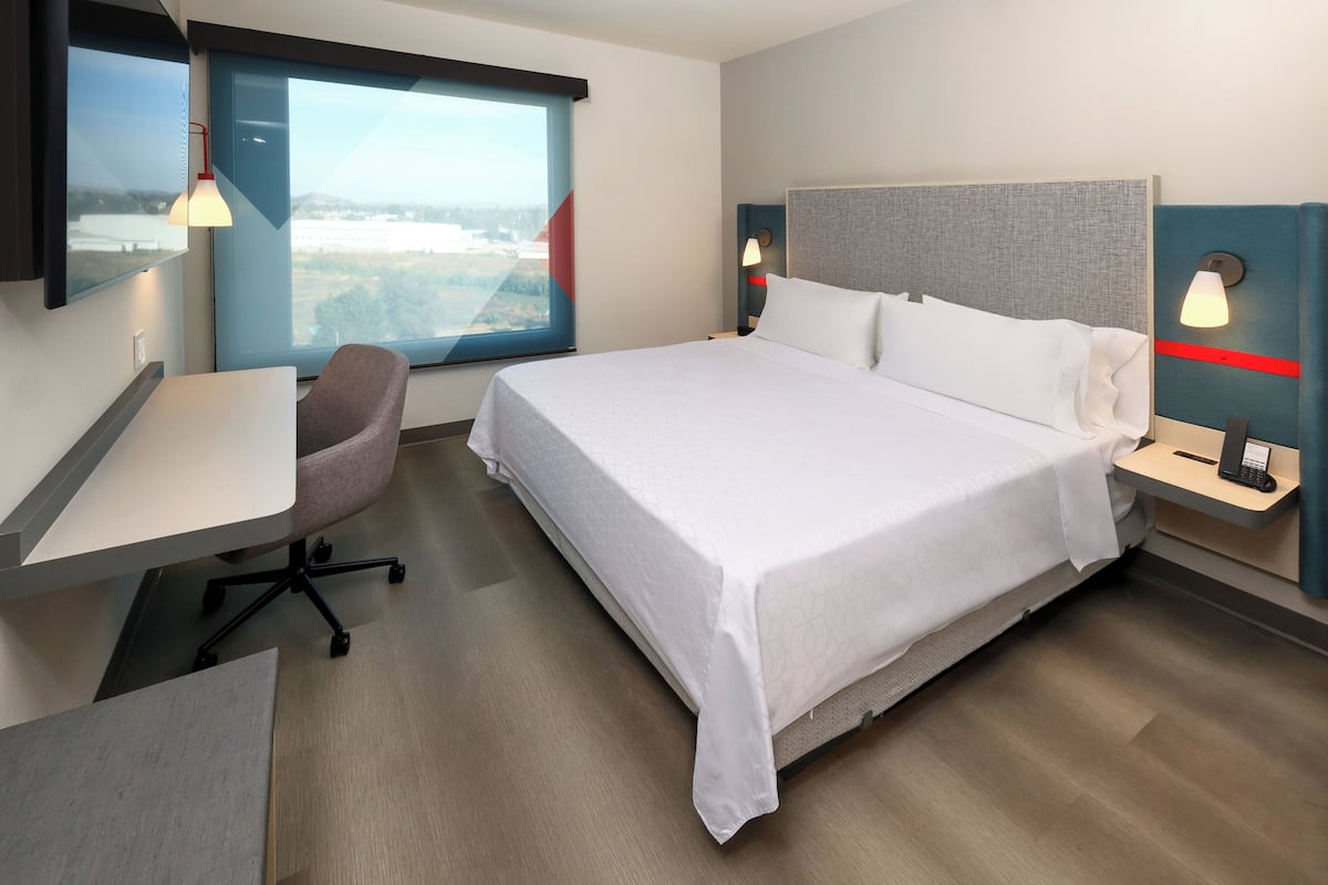 Ein Hotelzimmer mit einem großen Bett, einem Schreibtisch, einem Sessel und Blick auf die Stadt.