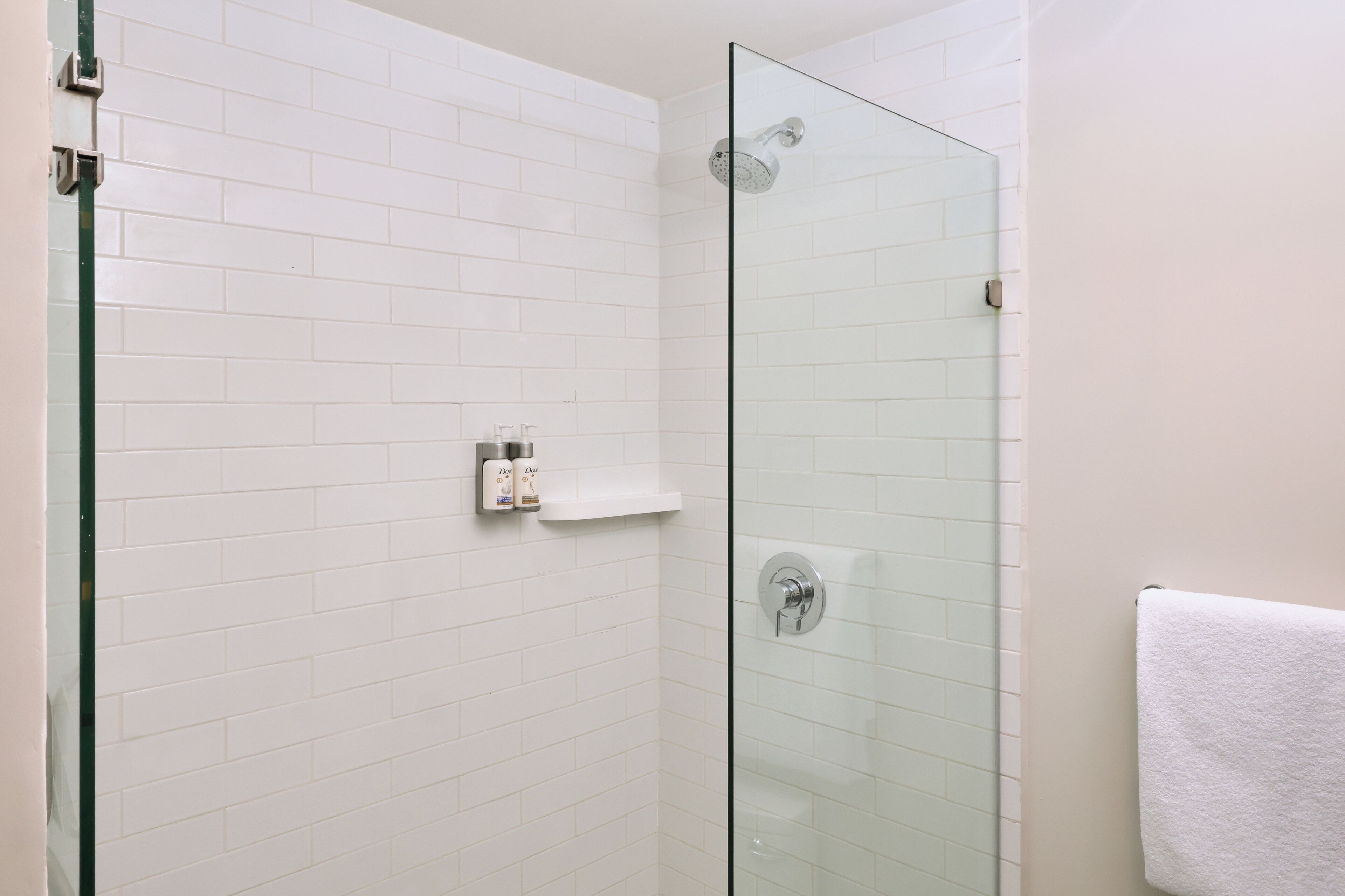 A modern bathroom with white tiled walls, a glass shower enclosure, and a white towel hanging on the wall.