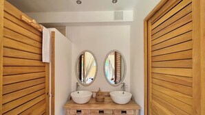 Une salle de bain avec un lambris en bois, deux miroirs ronds, un meuble-lavabo en bois avec deux vasques et une serviette accrochée au mur.