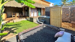 Un espace extérieur doté d’un toit de chaume, d’un jacuzzi, d’un mur en pierre et d’une terrasse en bois.