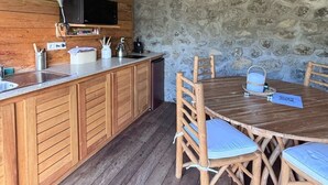 Un intérieur rustique avec des éléments en bois, un mur en pierre, des meubles de rangement en bois, une table à manger avec des chaises et un luminaire suspendu.
