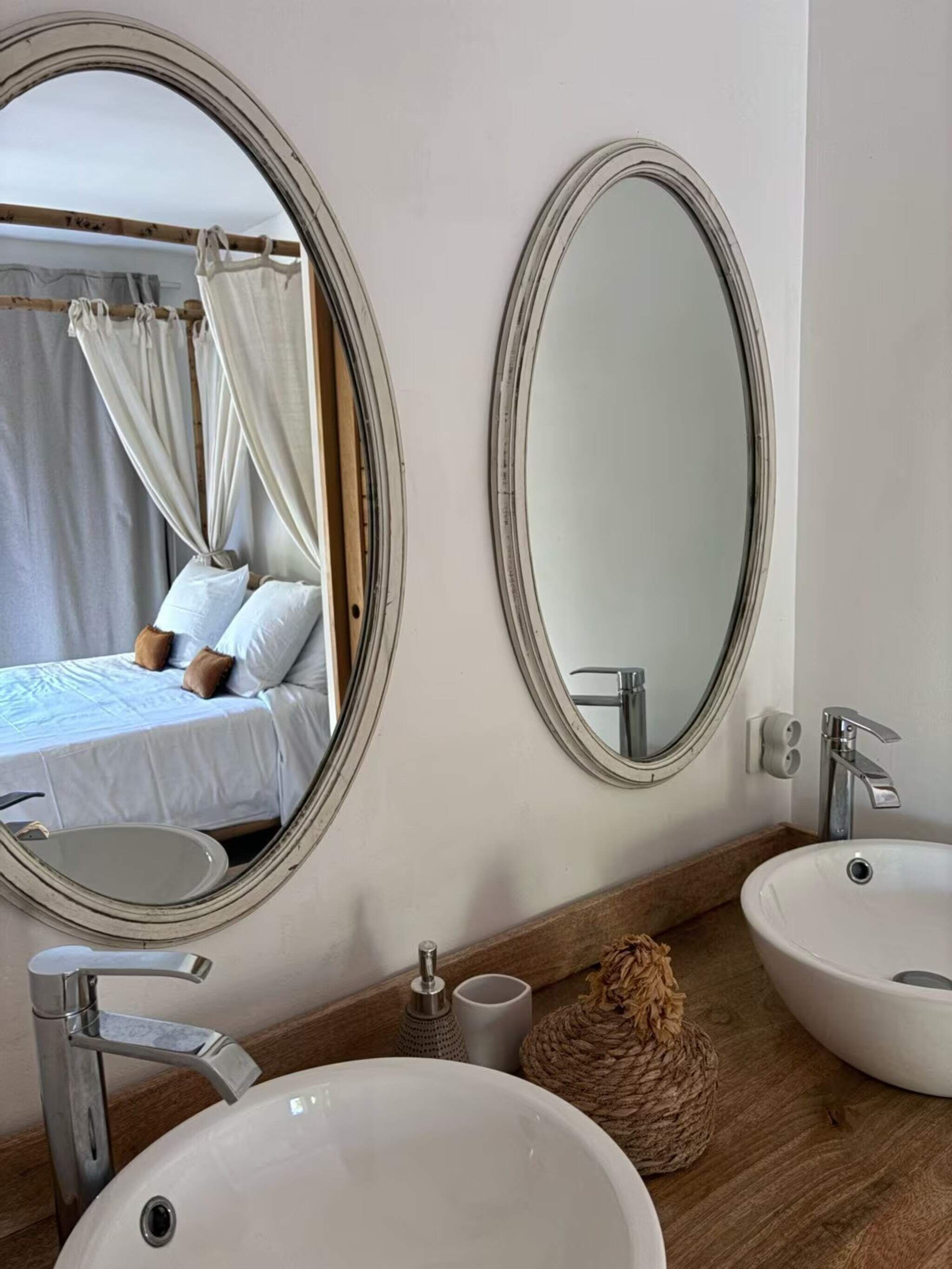 Un baño con dos espejos redondos, un tocador de madera y una cama con dosel.