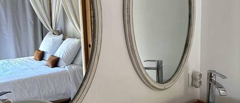 Un baño con dos espejos redondos, un tocador de madera y una cama con dosel.