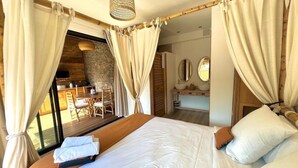 Une chambre avec un grand lit, des rideaux, un plafond en bois et une vue sur l’espace repas.