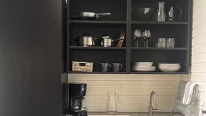 A kitchen with dark cabinets, a stainless steel sink, and various kitchenware including pots, pans, and glassware.
