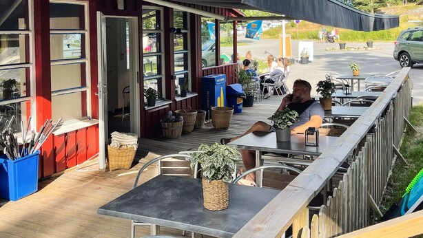 An outdoor seating area with tables and chairs, a covered section with a blue sign, and a view of the street.