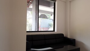 A room with a black sofa, a small table, and a window with a view of a building and greenery outside. - Casa Wyna family Ayur center (Mananthavady)