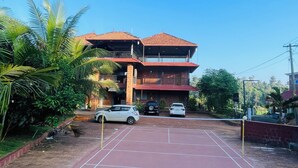 A multi-story building with a red-tiled roof, surrounded by greenery and parked cars. - Casa Wyna family Ayur center (Mananthavady)