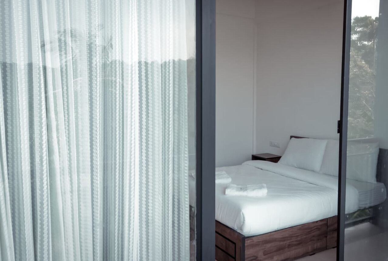 A bedroom with a wooden bed, white bedding, and sheer curtains.